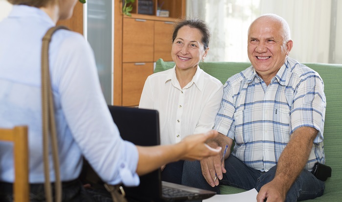 Mature happy couple filling questionnaire for employee with laptop of the bank